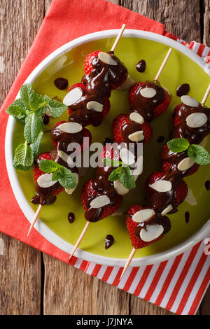 Estate fragole dessert con cioccolato, menta e mandorle close-up su una piastra. Vista verticale da sopra Foto Stock