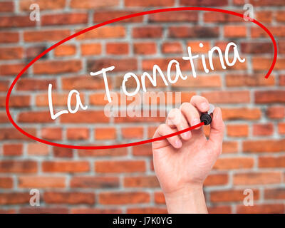 Man mano che scrive La Tomatina con pennarello nero su schermo visivo. Isolato su mattoni. Business, tecnologia internet concetto. Foto Stock