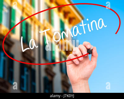 Man mano che scrive La Tomatina con pennarello nero su schermo visivo. Isolato sulla città. Business, tecnologia internet concetto. Foto Stock