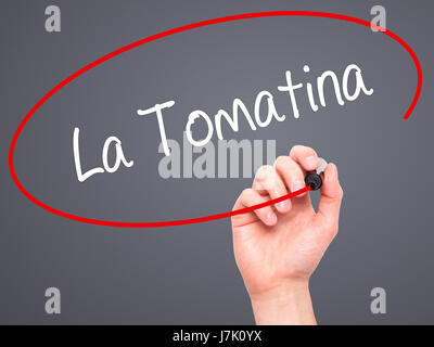 Man mano che scrive La Tomatina con pennarello nero su schermo visivo. Isolato su grigio. Business, tecnologia internet concetto. Foto Stock