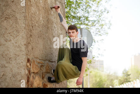 Giovane uomo appeso alla parete. Parkour nello spazio urbano. Sport in città. Attività sportive Foto Stock