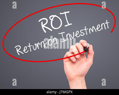 Man mano che scrive il ROI del ritorno sugli investimenti con pennarello nero su schermo visivo. Isolato su grigio. Business, tecnologia internet concetto. Stock Photo Foto Stock