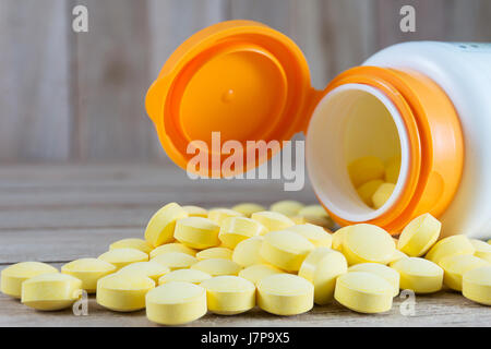 Pillole di giallo in bottiglia di plastica su uno sfondo di legno Foto Stock