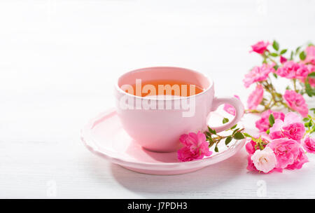 Tazza di tè e la filiale di piccole rose rosa sul tavolo rustico. Foto Stock