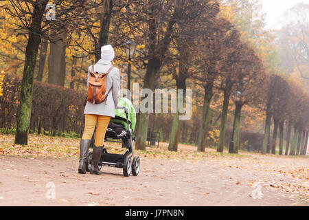 Donna che cammina in autunno park con il passeggino Foto Stock