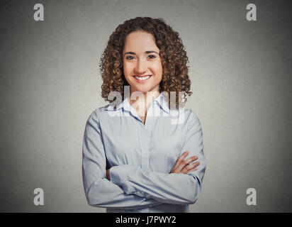 Closeup ritratto, felice, fiducioso, successo professionale di giovane donna in maglietta blu con le braccia incrociate piegato isolato muro grigio Sfondo. Positivo Foto Stock