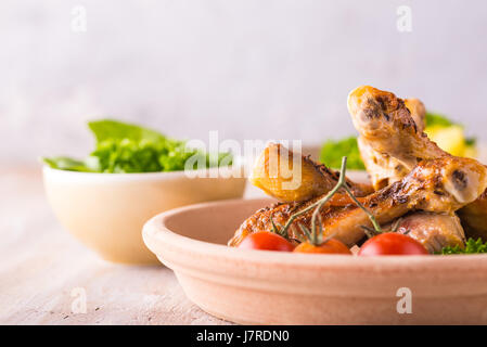 Foto orizzontale con tre bocce. La prima contiene il pollo al forno le gambe con la pelle croccante, il prezzemolo e i pomodori. La seconda maglia di patate alle erbe e uno con Foto Stock