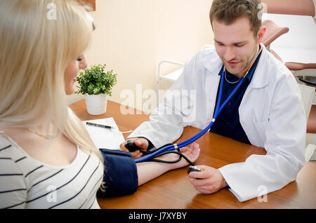 Giovane medico controllando la pressione del sangue del paziente femmina. La pressione del sangue del paziente medico medico sfigmomanometro di cuore il concetto di misurazione Foto Stock