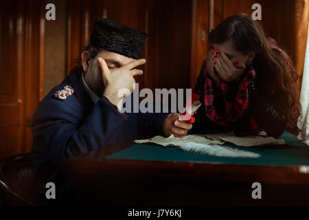 L'uomo e di una donna che piange sulle lettere che copre il viso con le mani. La donna in background al di fuori della messa a fuoco. Essi abiti retrò. Foto Stock
