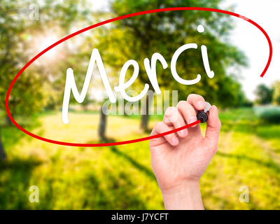 Man mano che scrive Merci (grazie in francese) con pennarello nero su schermo visivo. Isolato su sfondo. Business, tecnologia internet concetto. Stoc Foto Stock