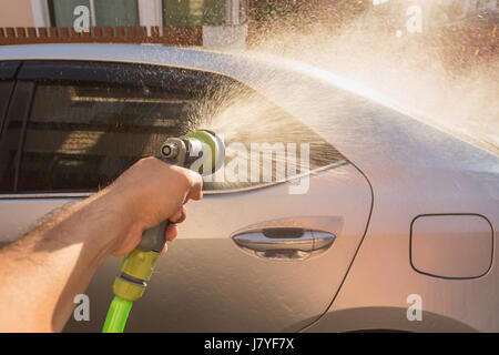 Chiudere la mano la spruzzatura di acqua di lavaggio auto. Auto privata e lavaggio. Focus sulla pistola a spruzzo Foto Stock