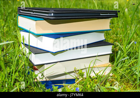 Pila di libri vari plus tablet nel fresco verde erba. Foto Stock