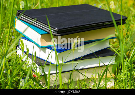 Pila di libri vari plus tablet nel fresco verde erba. Foto Stock