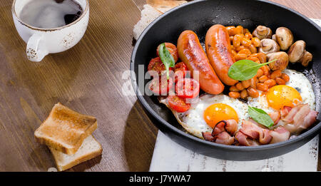 La completa prima colazione Inglese con uova fritte, salsicce, pancetta, fagioli, pane tostato e caffè. Foto Stock