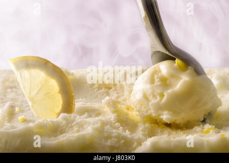 Rendere il gelato al limone sfera vicino. Vista frontale del contenitore per gelato e scoop prelievo di prodotti con frutta. Con vapore freddo in background. Parte anteriore Foto Stock