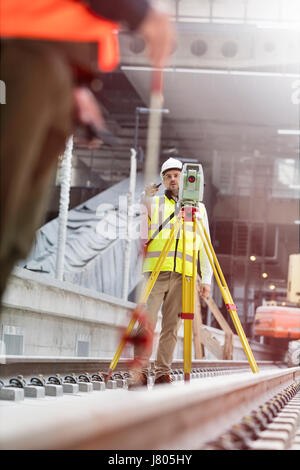 Ingegnere maschio utilizzando teodolite sulle vie al sito in costruzione Foto Stock