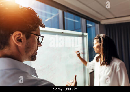 I colleghi per discutere dei piani aziendali in ufficio. Imprenditrice presentare idee su una lavagna mentre imprenditore a discutere con lei. Foto Stock