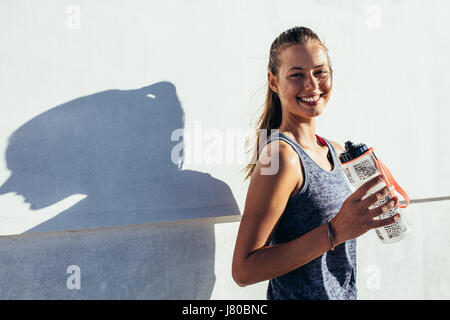 Colpo di happy runner all'aperto in piedi tenendo la bottiglia di acqua e sorridente. Donna Fitness prendendo una pausa dopo allenamento. Foto Stock