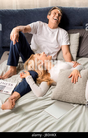Felice Coppia di mezza età ridere e giacente sul letto di casa Foto Stock