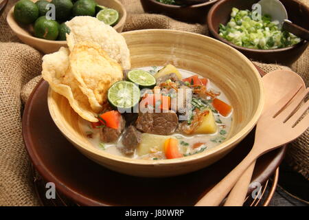 Soto Betawi, popolare carne in latte di cocco zuppa da Giacarta. Servita con pomodori, sedano, scalogno, scalogno, cracker, e calce. Foto Stock