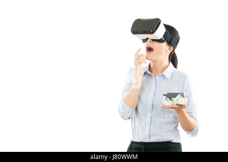 Eccitato giovane donna di Office utilizzando un auricolare VR e vivendo la realtà virtuale isolato su sfondo bianco che mostra house design modello e sorpreso o Foto Stock