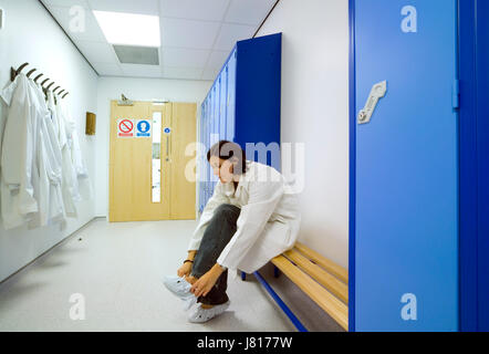 Una donna scienziato mette in soprascarpe in spogliatoio prima di entrare in un laboratorio sterile. Foto Stock