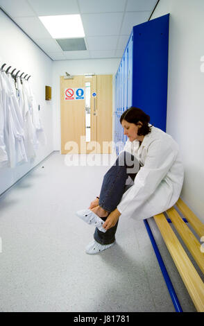 Una donna scienziato mette in soprascarpe in spogliatoio prima di entrare in un laboratorio sterile. Foto Stock