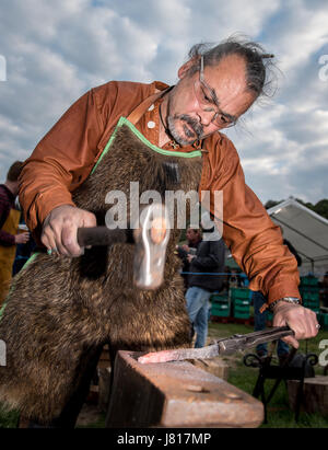 Un tradizionale swordsmith storico utilizzando i metodi e gli strumenti a percussione metallo in corrispondenza di un'incudine per rendere una spada presso il Festival di Beltain a Butser antica fattoria Foto Stock