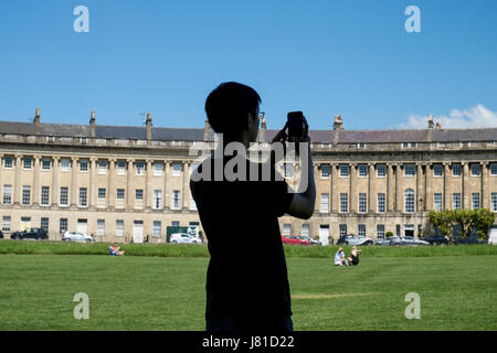 Bath, Regno Unito. 26 Maggio, 2017. Come bagno gode di un altro calda e soleggiata giornata un uomo in piedi all'ombra di un albero è raffigurato come utilizza il suo cellulare per scattare una fotografia del Royal Crescent. Credito: lynchpics/Alamy Live News Foto Stock