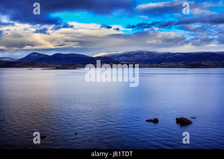 Jindabyne lago in montagna innevata inverno regione del NSW in Australia a sunrise. Distante innevate vette sotto il cielo blu e nuvole temporalesche r Foto Stock