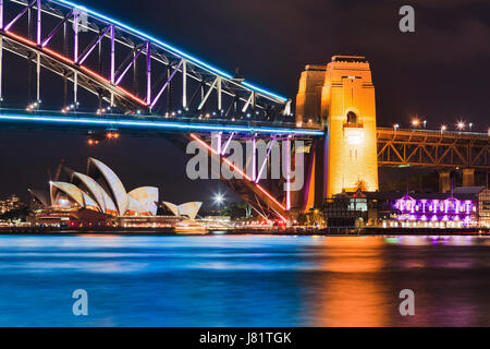 Vivida luce di Sydney e idee mostra tutto sfocato nelle acque del porto con i principali punti di riferimento della città e Harbour Bridge che riflette in pieno l'illuminazione. Foto Stock