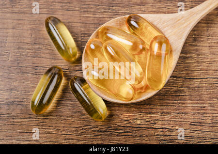 Olio di pesce di capsule con omega 3 e vitamina D con un cucchiaio di legno su legno texture, dieta sana nozione. Foto Stock