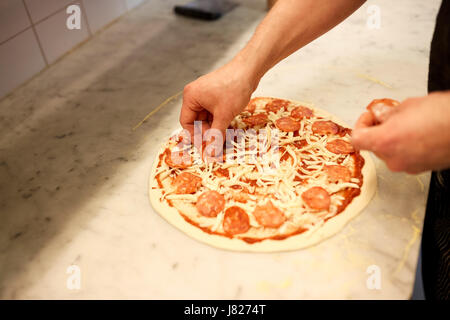 Cuocere le mani aggiungendo salami di pizza in pizzeria Foto Stock