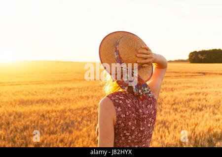 Vista posteriore di una ragazza in piedi nel campo giallo e godersi l'estate in natura, ora d'oro, tramonto Foto Stock