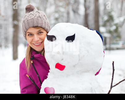 Immagine di una bella ragazza in posa accanto a un pupazzo di neve Foto Stock