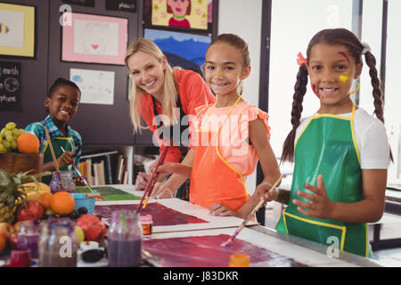 Ritratto del maestro sorridente e schoolkids in piedi in aula di disegno Foto Stock