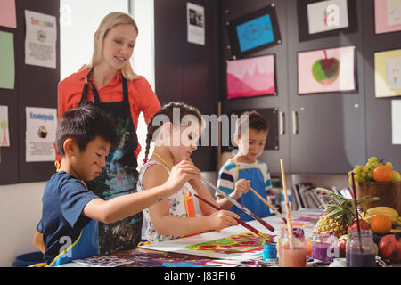 Insegnante assistere schoolkids nella classe di disegno a scuola Foto Stock