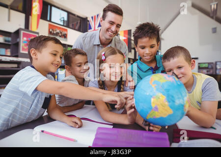 Insegnante assistere schoolkids sul globo terrestre in libreria Foto Stock