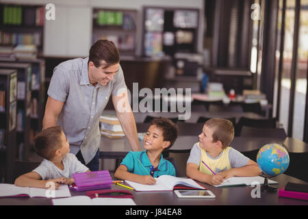 Insegnante aiutando schoolkids con i loro compiti in biblioteca a scuola Foto Stock