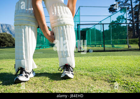 Sezione bassa del giocatore di cricket kneedpad legatura mentre si sta in piedi sul campo erboso Foto Stock