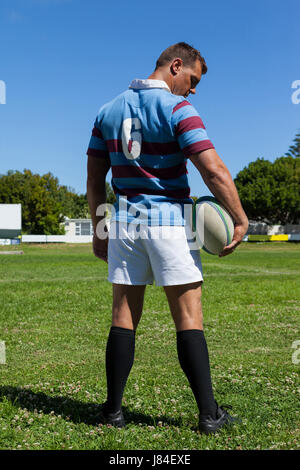 Vista posteriore del rugby giocatore in possesso palla mentre permanente al campo da gioco durante la giornata di sole Foto Stock