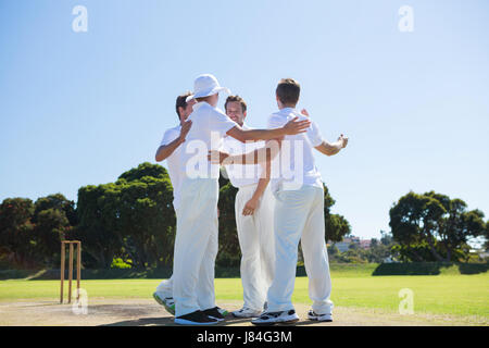 Sorridente giocatori di cricket in piedi in campo contro il cielo chiaro Foto Stock