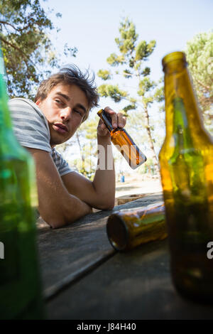 Inconscio uomo beve birra dalla bottiglia nel parco Foto Stock