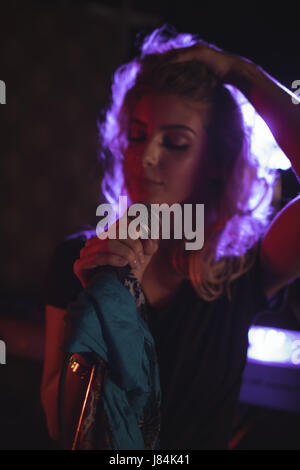 Bellissima cantante femminile con le mani nei capelli eseguendo in discoteca illuminata Foto Stock