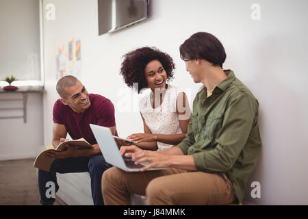 Happy business i colleghi che lavorano insieme mentre è seduto da parete in ufficio creativo Foto Stock