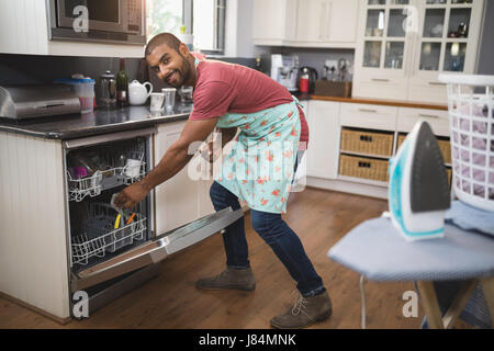 Ritratto di giovane sorridente uomo mettendo utensili in lavastoviglie in cucina Foto Stock