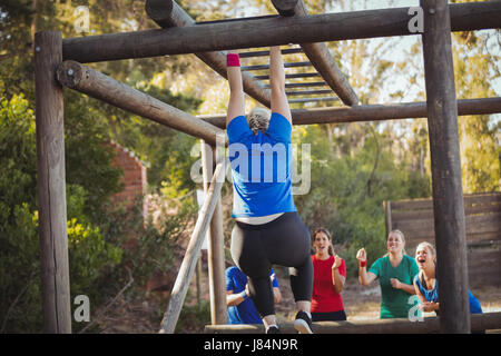 Donna di essere acclamato bye i suoi compagni di squadra a salire Monkey bar durante la corsa a ostacoli della formazione in boot camp Foto Stock