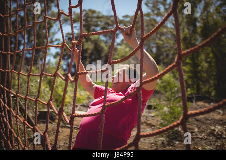 Determinata donna scalata di un net durante il percorso ad ostacoli in boot camp Foto Stock