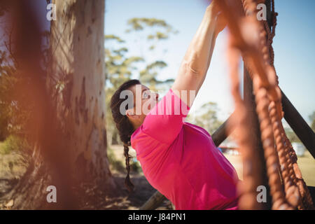 Determinata donna scalata di un net durante il percorso ad ostacoli in boot camp Foto Stock