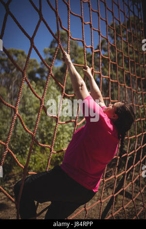 Determinata donna scalata di un net durante il percorso ad ostacoli in boot camp Foto Stock